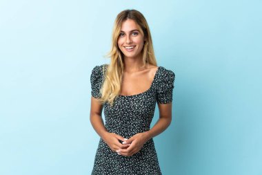 Genç sarışın Uruguaylı, mavi arka planda tek başına gülüyor.