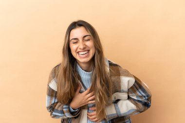 Beyaz tenli genç bir kadın, bej arka planda izole edilmiş, gülümsüyor.