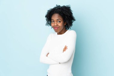 Genç Afrikalı Amerikalı kadın mavi arka planda izole edilmiş. Omuzlarını kaldırırken şüphe jestleri yapıyor.