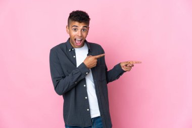 Pembe arka planda izole edilmiş genç Brezilyalı adam şaşırmış ve işaret ediyor.
