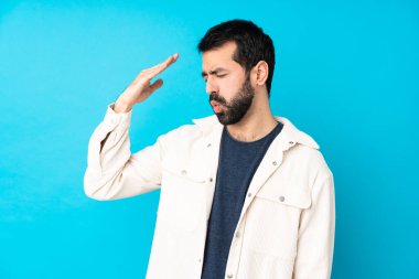 Beyaz kadife ceketli genç yakışıklı adam, izole edilmiş mavi arka planda, yorgun ve hasta bir ifadeyle.