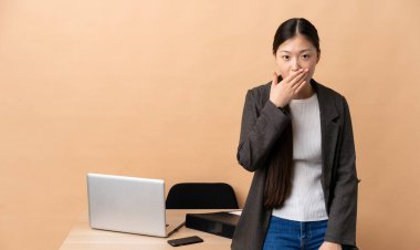 İş yerindeki Çinli iş kadını mutlu ve gülümsüyor. Ağzını eliyle kapatıyor.