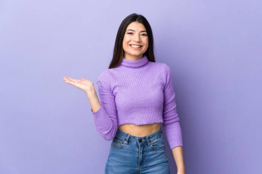 İzole edilmiş mor arka planda genç esmer kadın bir ilan vermek için avucunun içinde hayali bir mekan tutuyor.