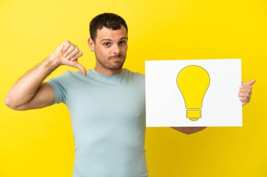 İzole edilmiş mor arka plan üzerinde Brezilyalı bir adam elinde gururlu bir jestli ampul simgesi olan bir levha tutuyor.