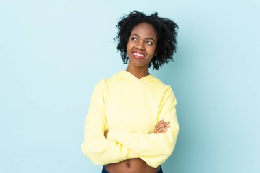 Genç Afrikalı Amerikalı kadın mavi arka planda izole edilmiş gülümserken yukarı bakıyor