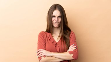 Beyazlı genç bir kadın, mutsuz bir ifadeyle bej arka planda izole edilmiş.