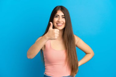 Mavi arka planda izole edilmiş beyaz bir kadın baş parmak işareti yapıyor.