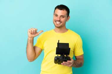 İzole edilmiş mavi arka plan üzerinde uzaktan kumandayı elinde tutan Brezilyalı adam gururlu ve kendinden memnun.