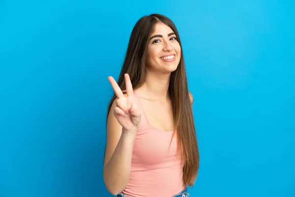 Jonge Kaukasische Vrouw Geïsoleerd Blauwe Achtergrond Glimlachen Tonen Overwinning Teken — Stockfoto