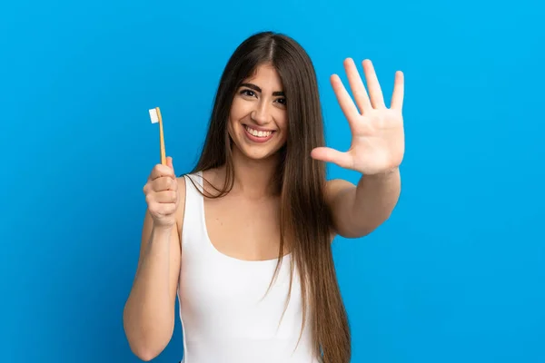 Młoda Biała Kobieta Myje Zęby Odizolowane Niebieskim Tle Licząc Pięć — Zdjęcie stockowe