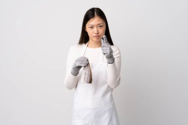 Çinli balıkçı önlük takıyor ve çiğ balığı izole edilmiş beyaz arka planda tutuyor hayal kırıklığına uğramış ve ön tarafı gösteriyor.