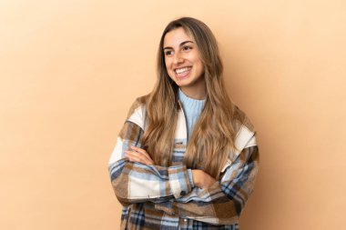 Beyaz tenli genç bir kadın bej arka planda izole edilmiş mutlu ve gülümsüyor.