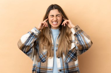 Beyazların arka planında izole edilmiş genç beyaz kadın hayal kırıklığına uğramış ve kulaklarını kapatmış.