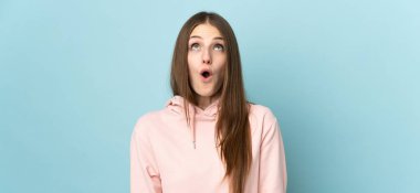 Genç beyaz kadın mavi arka planda izole edilmiş yukarı bakıyor ve şaşırmış bir ifadeyle