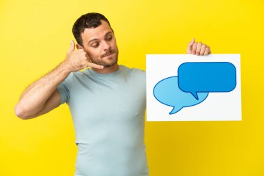 İzole edilmiş mor arka plan üzerinde Brezilyalı bir adam elinde konuşma balonu ikonu olan bir levha tutuyor ve telefon jesti yapıyor.