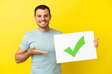 İzole edilmiş mor arkaplan üzerinde Brezilyalı bir adam. Üzerinde yeşil işaret simgesi olan bir levha tutuyor ve onu işaret ediyor.