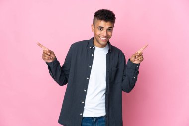 Pembe arka planda izole edilmiş genç Brezilyalı adam parmak uçlarını işaret ediyor ve mutlu.