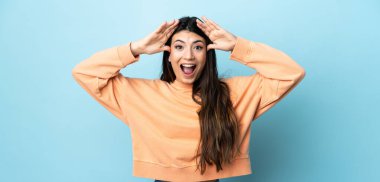 Genç esmer kız, izole edilmiş mavi arka planda sürpriz bir ifadeyle.