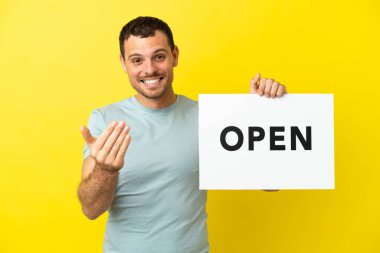 Mor arka planda Brezilyalı bir adam. Elinde açık yazılı bir levha var.