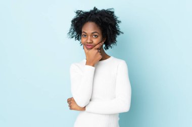 Genç Afrikalı Amerikalı kadın, mavi arka planda izole edilmiş. Şüpheleri var.