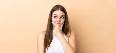 Kafkasyalı genç bir kadın bej arka planda izole edilmiş. Şüpheleri var ve kafası karışmış bir yüz ifadesi var.