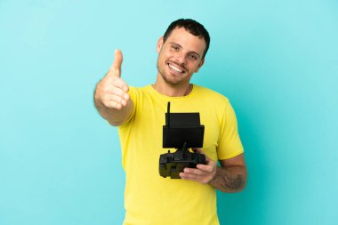 Brezilyalı bir adam, izole edilmiş mavi arka plan üzerinde uzaktan kumanda tutuyor ve iyi bir anlaşma için el sıkışıyor.