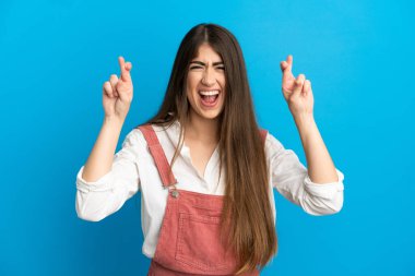 Genç beyaz kadın, mavi arka planda izole edilmiş ve şans diliyor.