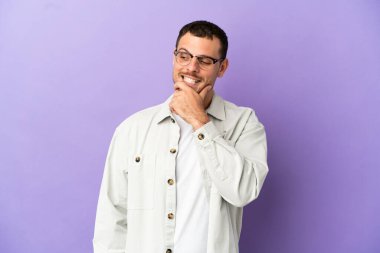 İzole edilmiş mor arka planı olan Brezilyalı bir adam yana bakıyor ve gülümsüyor.