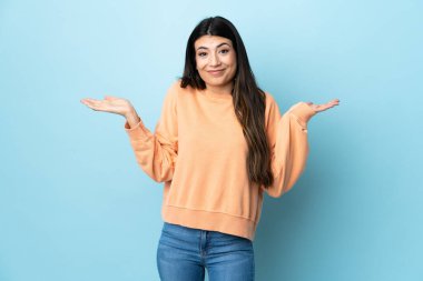 Genç esmer kız soyutlanmış mavi arka planda şüpheleri varken el kaldırıyor.