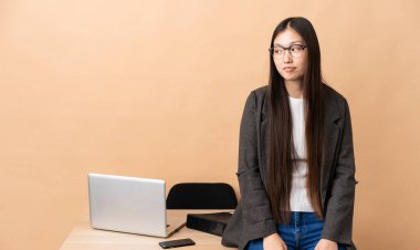 Chinese business woman in her workplace making doubts gesture looking side