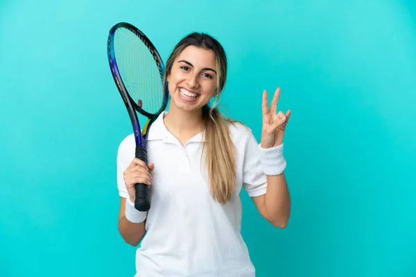 Ung Kvinde Tennisspiller Isoleret Blå Baggrund Smilende Viser Sejr Tegn - Stock-foto