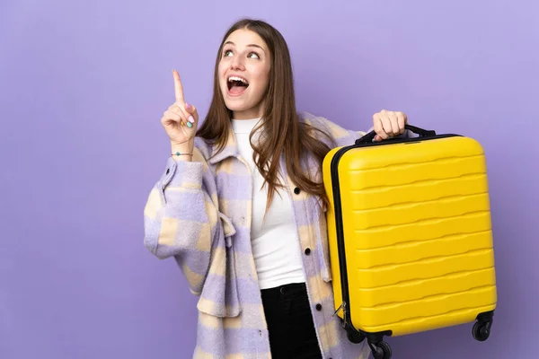 年轻的高加索女人穿着紫色背景的衣服 带着旅行箱和指尖 在度假时被隔离在外 — 图库照片