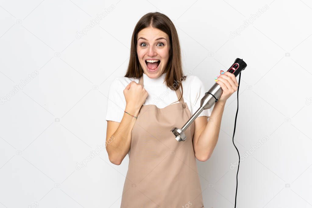 Young woman using hand blender isolated on white background celebrating a victory
