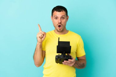 İzole edilmiş mavi arkaplan üzerinde uzaktan kumandayla uzaktan kumanda tutan Brezilyalı bir adam çözümü bulmak için parmağını kaldırıyor.