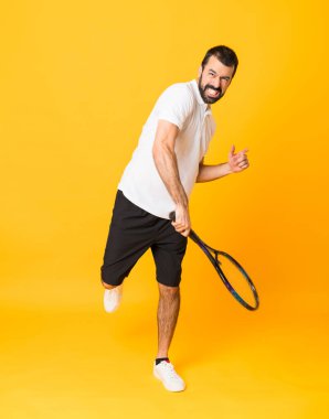 İzole edilmiş sarı arka planda tenis oynayan bir adamın tam boy çekimi.