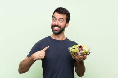 Yeşil duvarın üstünde salata salatası olan yakışıklı genç bir adam.