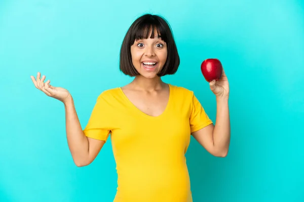 Schwangere Mit Einem Apfel Auf Blauem Hintergrund Und Schockiertem Gesichtsausdruck — Stockfoto