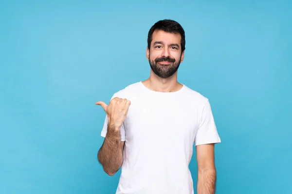 Ung Man Med Skägg Över Isolerad Blå Bakgrund Pekar Sidan — Stockfoto