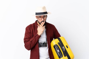 Sakallı bir gezgin, izole edilmiş beyaz arka planda gözlüklü bir bavul tutuyor ve şaşırıyor.