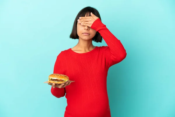 Młoda Ciężarna Kobieta Trzymająca Hamburgera Nad Odosobnionym Tłem Zakrywającym Oczy — Zdjęcie stockowe