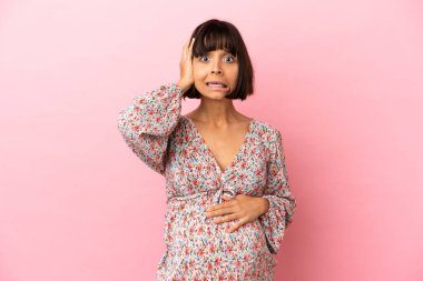 Genç hamile bir kadın pembe arka planda gergin hareketler yapıyor.