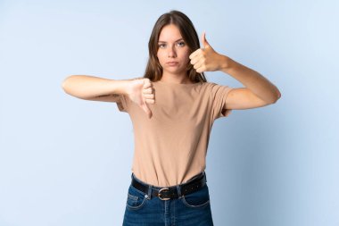 Genç Litvanyalı kadın mavi arka planda izole edilmiş, iyiye kötüye işaret yapıyor. Evet ya da hayır arasında kararsız