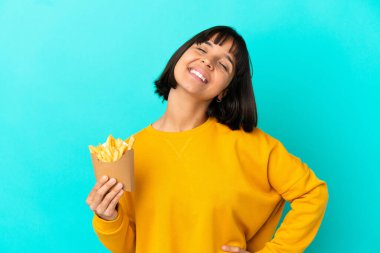 Genç esmer kadın izole edilmiş mavi arka planda kızarmış patates kızartması tutuyor.