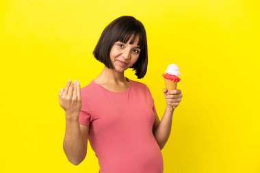 Kornet dondurması tutan hamile bir kadın sarı arka planda izole edilmiş bir şekilde elini uzatmaya davet ediyor. Gelmene sevindim.