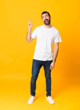 Sarı arka planda sakallı bir adamın tam boy fotoğrafı. Çözümü bulmak için parmağını kaldırıyor.