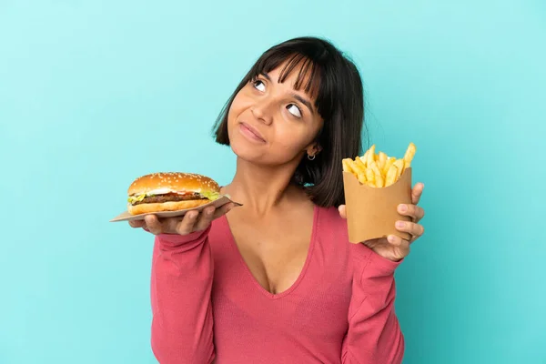 Νεαρή Μελαχρινή Γυναίκα Κρατώντας Burger Και Τηγανητές Πατάτες Απομονωμένο Μπλε — Φωτογραφία Αρχείου