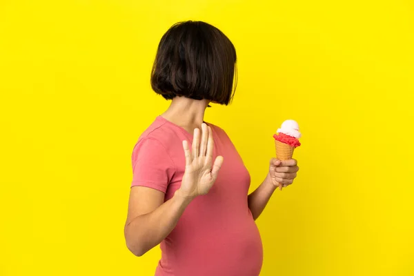 妊娠中の女性を保持していますコーネットアイスクリーム隔離上の黄色の背景作りストップジェスチャーと失望 — ストック写真