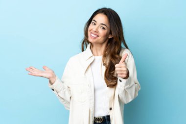 Woman over isolated background holding copyspace imaginary on the palm to insert an ad and with thumbs up