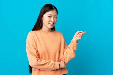 İzole edilmiş mavi arka planda genç bir Çinli kız parmak kaldırıyor.