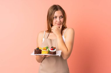 Ukraynalı aşçı pembe arka planda izole edilmiş bir kek tutarak bir fikir düşünüyor.